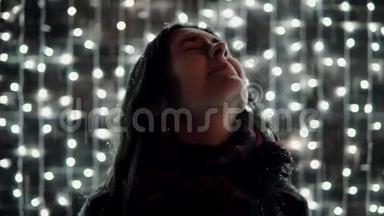 年轻漂亮的女人，在<strong>装饰墙</strong>前的圣诞夜里，享受着降雪，满是闪闪发光的灯光